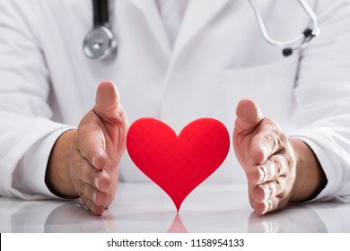 Doctor's Hand Protecting Red Heart On Desk