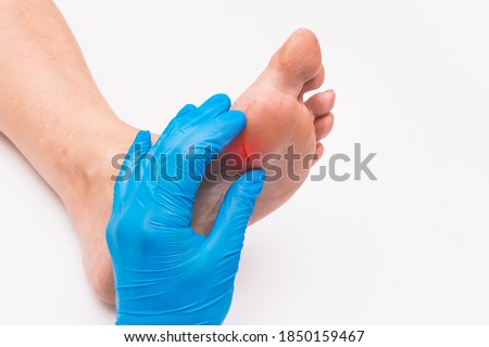 Doctor's hand in a protective medical glove touches and examines the wound on the foot of an elderly woman on a white background