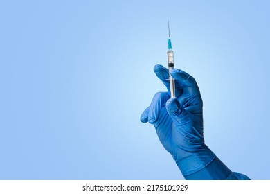 Doctors hand in surgical gloves holds a syringe on a classic symbolic blue background - Shutterstock ID 2175101929