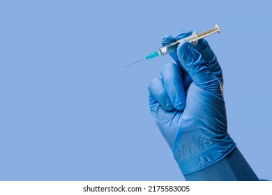 Doctors hand in surgical gloves holds a syringe on a classic symbolic blue background - Shutterstock ID 2175583005