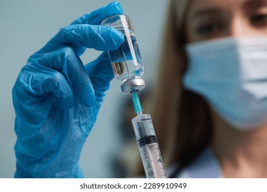 The doctor's hand wears a medical glove holding a syringe while taking a liquid vaccine from a vial about to be injected. Injection vaccination concept - Powered by Shutterstock