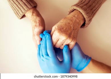 A doctor's hands in a blue gloves holds the hands of an elderly woman, a patient. Handshake, caring, trust and support. Medicine and healthcare.