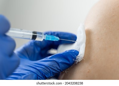 A Doctor's Hands In Blue Medical Gloves Give A Tetanus Shot To A Patient's Shoulder Through A Disinfected Bandage. The Syringe Bites Into The Patient's Skin.