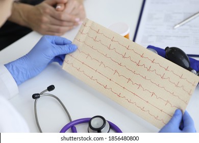 Doctor's hands hold result of the cardiogram next to patient sitting. Examination of the cardiovascular system concept. - Shutterstock ID 1856480800