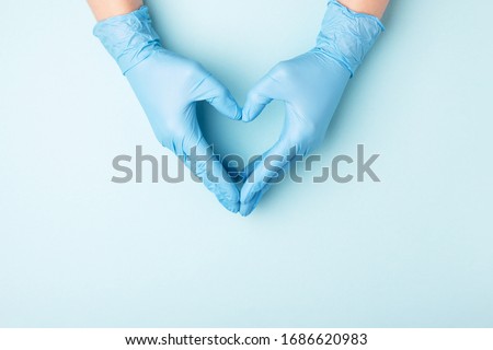 Doctor's hands in medical gloves in shape of heart on blue background with copy space.