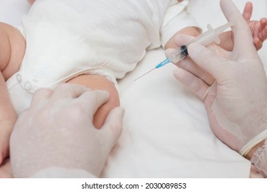 The Doctor's Hands In Rubber Protective Gloves Hold A Syringe. An Infant Receiving The Vaccine In The Leg. Visit To The Pediatrician In The Hospital. A Two-month-old Baby. To Close.