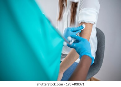 Doctor's hands in surgical gloves preparing COVID-19 vaccine for female patient. Female doctor wearing blue latex gloves injecting a woman in her arm with a needle and syringe  - Shutterstock ID 1937408371