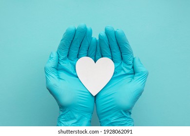 Doctors hands wearing blue surgical gloves holding a white heart shape