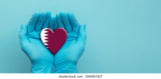 Doctors hands wearing surgical gloves holding Qatar flag heart