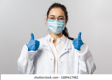 Doctors, infectionist, research and covid19 concept. Satisfied young asian female doctor receive good results on studying virus, discover vaccine, show thumb-up, wear face mask and gloves - Shutterstock ID 1689617482
