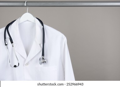 A doctor's lab coat and stethoscope on hanger against a gray background. Closeup on a white hanger with a gray background in horizontal format with copy space.
