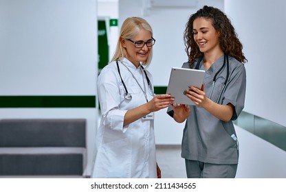 Doctors laugh and talk in the hallway. Older woman and young female doctors. - Shutterstock ID 2111434565