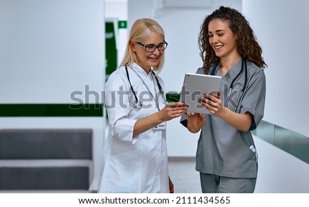 Doctors laugh and talk in the hallway. Older woman and young female doctors.