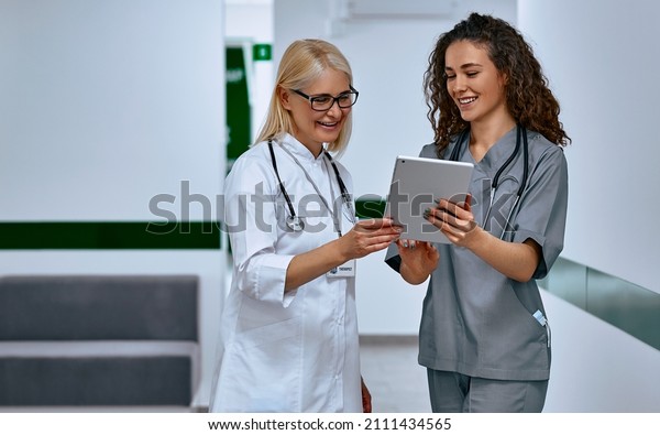 Doctors laugh and talk in the hallway. Older\
woman and young female\
doctors.