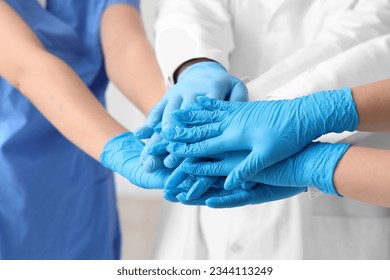 Médicos en guantes médicos juntando manos en la clínica, cerrando