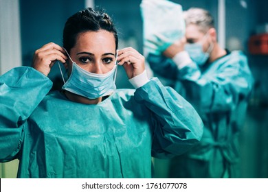 Doctors and nurse preparing to work in hospital for surgical operation during coronavirus pandemic outbreak - Medical workers getting dressed inside clinic - Focus on woman face protective mask