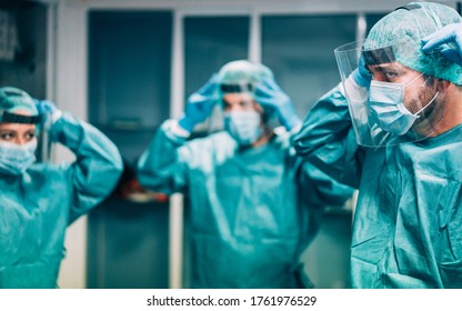 Doctors and nurse preparing to work in hospital for surgical operation during coronavirus pandemic outbreak - Medical workers getting dressed inside clinic - Focus on right man eye