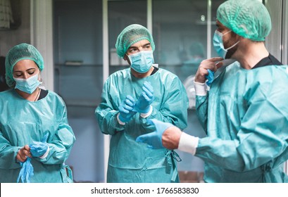 Doctors and nurse preparing to work in hospital for surgical operation during coronavirus pandemic outbreak - Medical workers getting dressed inside clinic - Focus on left man face