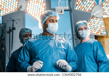 doctors and nurse in uniforms and medical masks looking away in operating room