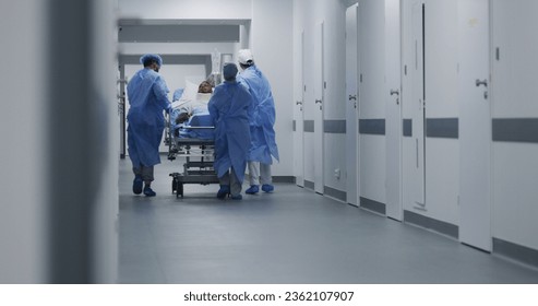 Doctors, nurses and paramedics push stretcher with patient to surgery room. African American man with neck brace lies on gurney. Multiracial staff work in emergency department. Slow motion. Back view. - Powered by Shutterstock