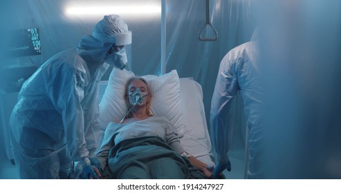 Doctors and nurses working hard to treat covid-19 infected patient in ICU. Medical staff in protective overall taking care of sick woman in oxygen mask lying on bed in isolation ward - Shutterstock ID 1914247927