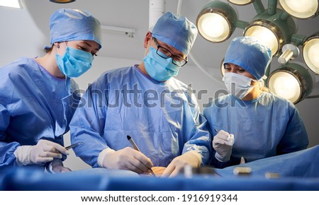 Doctors performing aesthetic surgery while patient lying on operating table. Surgeon and assistants performing cosmetic surgery in operating room. Concept of medicine, abdominoplasty, plastic surgery.