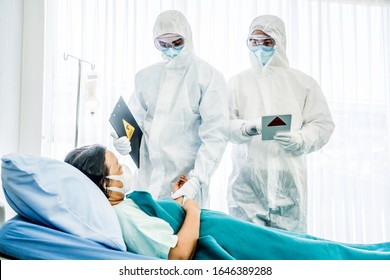 Doctors in the protective suits and masks are examining the infected aging female patient in the control area