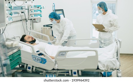 Doctors In Protective Suits And Masks Are Examining The Infected Coronavirus Young Man Patient In The Hospital Ward