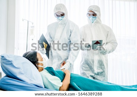 Doctors in the protective suits and masks are examining the infected aging female patient in the control area