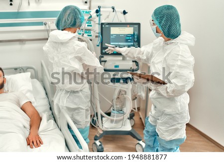 Doctors in protective suits and masks monitor the state of the intercourse of a patient with coronavirus disease covid-19 in the intensive care unit. Modern clinic.