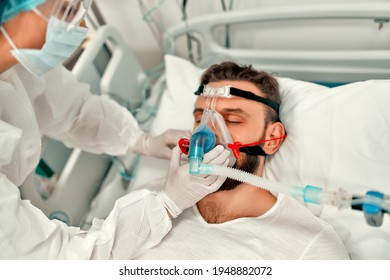 Doctors in protective suits put on a ventilation mask on a sick man with coronavirus disease covid-19, who is in an intensive care unit in a modern hospital. - Shutterstock ID 1948882072