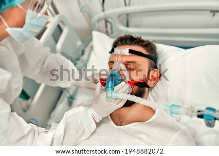 Doctors in protective suits put on a ventilation mask on a sick man with coronavirus disease covid-19, who is in an intensive care unit in a modern hospital.