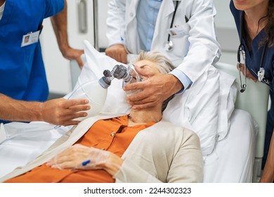 Doctors putting an oxygen mask on patient while rushing to operation theatre. Close up of nurse hand pumping oxygen in ambu bag mask during emergency. Team of emergency medical staff rescuing patient. - Powered by Shutterstock