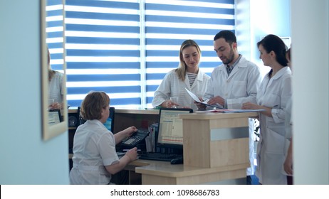 Doctors reviewing patient folders at hospital reception desk - Powered by Shutterstock