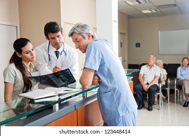 Doctors reviewing x-ray at hospital reception while people sitting in background - Powered by Shutterstock