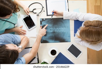 Doctors sitting around the table and interpreting x-ray image - Shutterstock ID 251466229