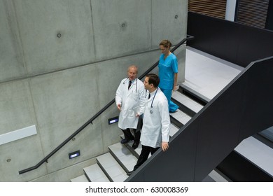 Doctors and surgeons interacting with each other on staircase in hospital - Powered by Shutterstock