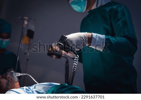 Doctors and team performing using defibrillator to give electrical shock wave to patient heart in bright Modern operating room with lighting equipment at hospital.