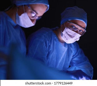 Doctors Team In Surgery In A Dark Background.