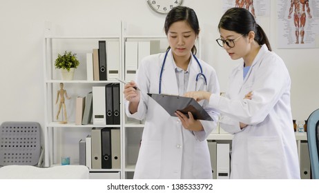 Doctors Woman In White Lab Coat Examining X-ray On Clipboard Having Discussion In Hospital Office. Young Girl Medical Staffs Talking About Patient Situation Surgery. Professional Teamwork In Clinic.