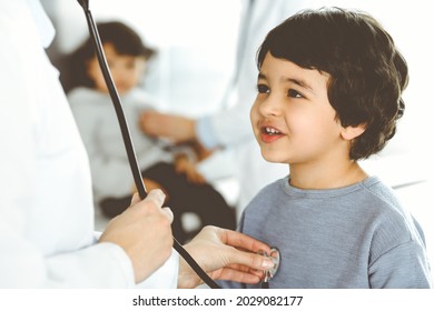 Doctor-woman examining a child patient by stethoscope. Cute arab boy and his brother at physician appointment. Medicine concept - Powered by Shutterstock