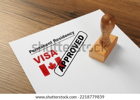 Document with approved permanent residency visa in Canada and stamp on wooden table
