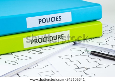 Document binders with POLICIES and PROCEDURE words on labels place on blank process flow charts with pen