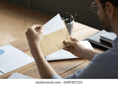Document delivery. Cropped close up young businessman sit at office desk hold envelop with paper letter in hands. Sending or receiving official notifications business correspondence paperwork concept