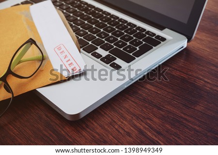 Document with denied stamp and laptop put on the wooden table.