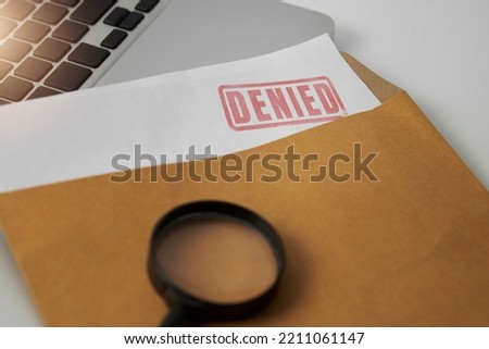 Document with denied stamp and magnifying glasses put on the laptop on wooden table,