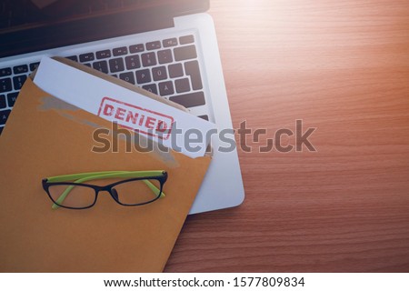 Document with denied stamp put on the laptop on wooden table,