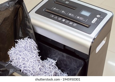 Document shredder with paper shreds on garbage black bag and tray garbage.