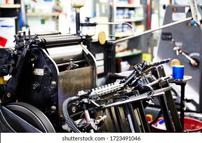 Documentary Photography Of A Commercial Printer: Detail Of A Heidelberg Printer With A Printing Workshop In The Background