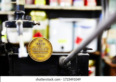 Documentary Photography Of A Commercial Printer: Detail Of A Heidelberg Printer With A Printing Workshop In The Background